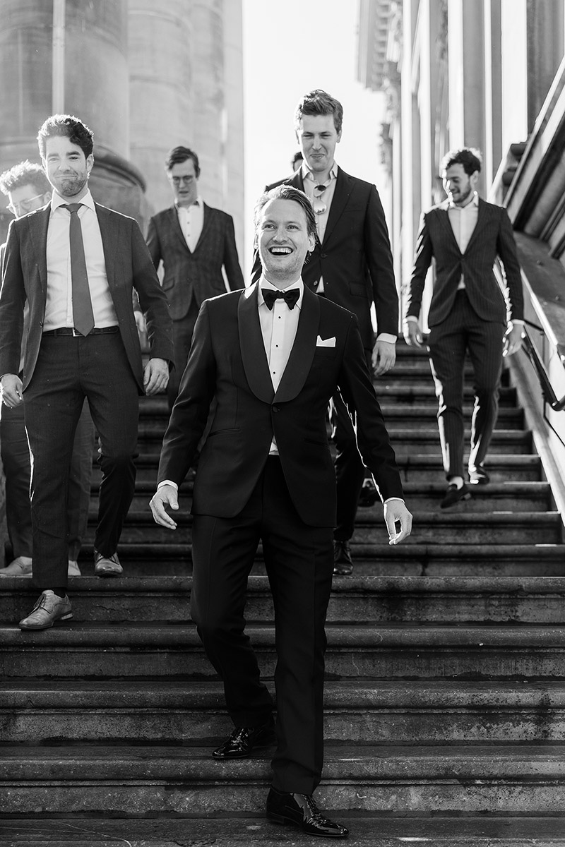 Bruidegom loopt lachend met zijn vrienden een trap af tijdens de trouwdag, vastgelegd in documentaire stijl