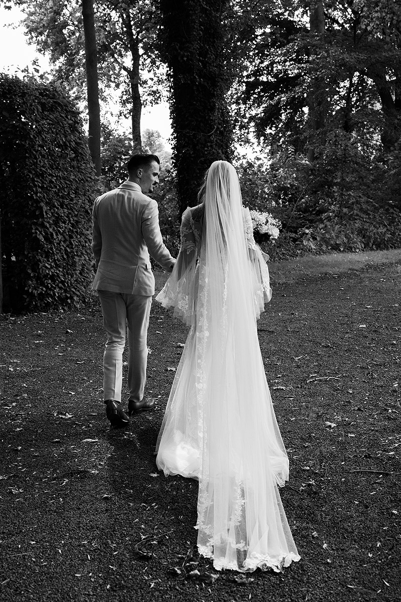 Wandelend bruidspaar tijdens de trouwshoot, begeleid en vastgelegd in een natuurlijke, editorial stijl